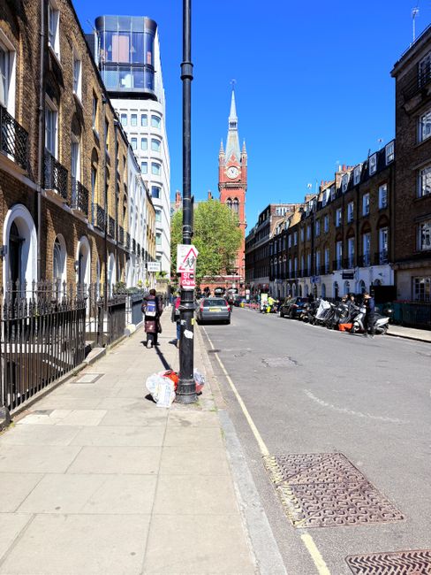 A busy street scene on Whitechapel Road E1 featuring a row of multi-storey residential buildings with brick facades, pitched roofs, and multiple windows, alongside ground-floor commercial units includ